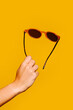 © VICTOR TORRES/Stocksy - Woman's hand holding sunglasses on yellow background