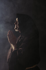 Canvas Print - side view of medieval monk in hooded cassock praying on black with smoke.