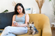 © nomad studio/Stocksy - Woman using a mobile phone sitting on a sofa with her dog.