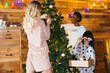 © BONNINSTUDIO/Stocksy - Diverse women smiling and decorating coniferous tree