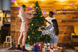© BONNINSTUDIO/Stocksy - Women decorating Christmas tree against wooden wall