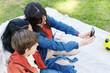 © Ivan Gener/Stocksy - Lesbian couple and their son taking selfies in a park