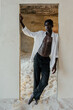 © Sergey Narevskih/Stocksy - African young man in doorway in minimal studio with sand