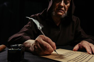 Sticker - blurred medieval monk writing manuscript with feather pen isolated on black.