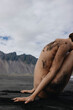 © Anastasia Mihaylova (Shpara)/Stocksy - Naked girl sitting on sand near the sea in front of mountains Iceland