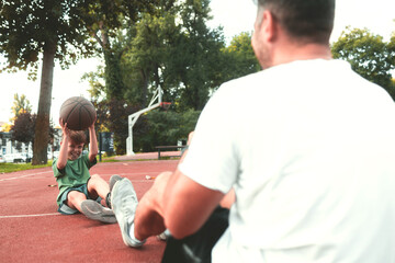 Wall Mural - Father and son  sit on a basketball court, throw a basketball at each other. Father helps his son with basketball training.