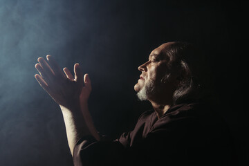 Wall Mural - side view of medieval priest praying on black background with smoke.