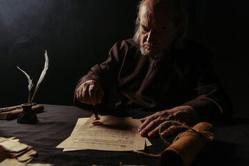 Wall Mural - ancient monk stamping manuscript with wax seal near rolled parchment isolated on black.