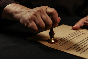 Poster - cropped view of monk stamping chronicle with wax seal isolated on black.