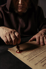Sticker - cropped view of priest putting wax seal on ancient chronicle isolated on black.