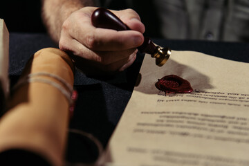 Canvas Print - partial view of medieval monk stamping manuscript with wax seal on blurred foreground and black surface.