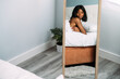 © David Prado/Stocksy - Black woman reflecting in mirror while lying on bed