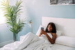 © David Prado/Stocksy - Black woman browsing smartphone on bed