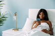 © David Prado/Stocksy - Black woman browsing smartphone on bed