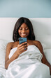 © David Prado/Stocksy - black woman using smartphone in bed