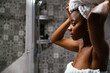 © David Prado/Stocksy - Black woman in towels standing in bathroom