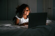 © David Prado/Stocksy - Smiling african woman using laptop in bed at night