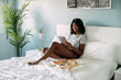 © David Prado/Stocksy - Black woman browsing tablet on bed