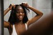 © David Prado/Stocksy - Smiling black woman putting on wig