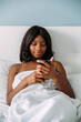 © David Prado/Stocksy - black woman using smartphone in bed