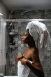 © David Prado/Stocksy - Black woman in towels standing in bathroom