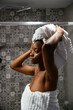© David Prado/Stocksy - Black woman in towels standing in bathroom