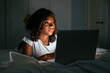 © David Prado/Stocksy - Smiling african woman using laptop in bed at night