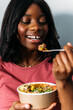 © David Prado/Stocksy - Cheerful black woman eating poke bowl
