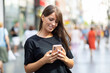 © Adam Radosavljevic - Beautiful smiling woman in black shirt texting on smartphone on street in city center