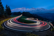 Light Trail Of Moving Cars Driving Up A Panoramic Serpentine Road In The Swiss Alps