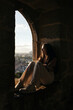 © Pedro Merino/Stocksy - Girl sitting on the window sill watching the city