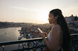 © Pedro Merino/Stocksy - Young woman using smartphone and watching the city from the bridge