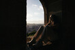 © Pedro Merino/Stocksy - Girl sitting on the window sill watching the city