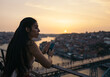 © Pedro Merino/Stocksy - Pretty young woman watching sunset and using smartphone
