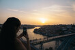 © Pedro Merino/Stocksy - Young woman taking pictures with smartphone of the sunset in Porto