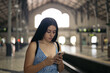 © Pedro Merino/Stocksy - Young woman waiting for the train at the station using smartphone
