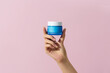 © Marc Tran/Stocksy - hand holding cosmetic face cream isolated on pink background.