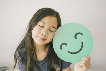 Wall Mural - Happy mixed Asian girl holding smile emoji face, positive mental health concept