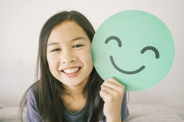 Wall Mural - Happy mixed Asian girl holding smile emoji face, positive mental health concept