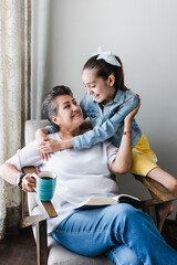 Wall Mural - hispanic Family granddaughter and grandmother reading a book, woman senior at home in Latin America