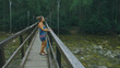 © ivandanru - Woman Walking Along Suspension Bridge Alone in Picturesque Green Forest Setting. Slow Motion of Dark Haired Woman Walk on Suspension Bridge in Thick Green Forest. No Other People Are in The Shot.