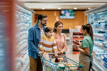 Happy family talks to saleswoman at diary products section in supermarket.