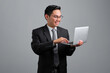 Portrait of smiling handsome young businessman in formal suit holding an open laptop in hand isolated on grey background