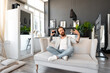 © fotofabrika - Positive bearded man listening music with headphones while sitting on couch at home