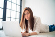 © themorningglory - Business asian woman lying on living room use laptop