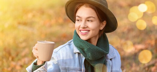 Wall Mural - Pretty young woman drinking hot tea in autumn park