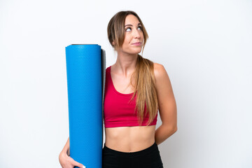 Canvas Print - Young sport woman going to yoga classes while holding a mat isolated on white background and looking up