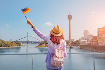 A young happy Asian girl with a German flag poses at the Media Harbor and TV-tower in Dusseldorf. Studying language abroad and traveling concept