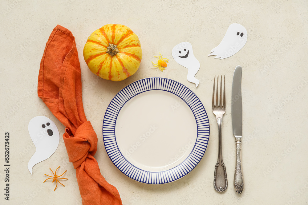 Table setting for Halloween celebration with paper ghosts and pumpkin on light background