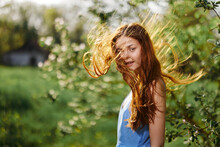 Woman With A Beautiful Smile With Teeth And Long Hair Flying Hair In The Spring Sunset In Nature In The Park Near The Flowering Trees Happiness, Natural Beauty And Hair Health
